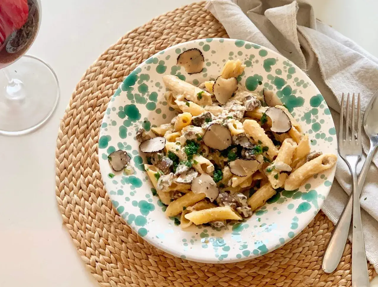 En tallrik med penne tryffelpasta, toppad med f&auml;rsk tryffel och persilja. Ett glas r&ouml;dvin st&aring;r bredvid, perfekt f&ouml;r att ackompanjera denna lyxiga r&auml;tt.