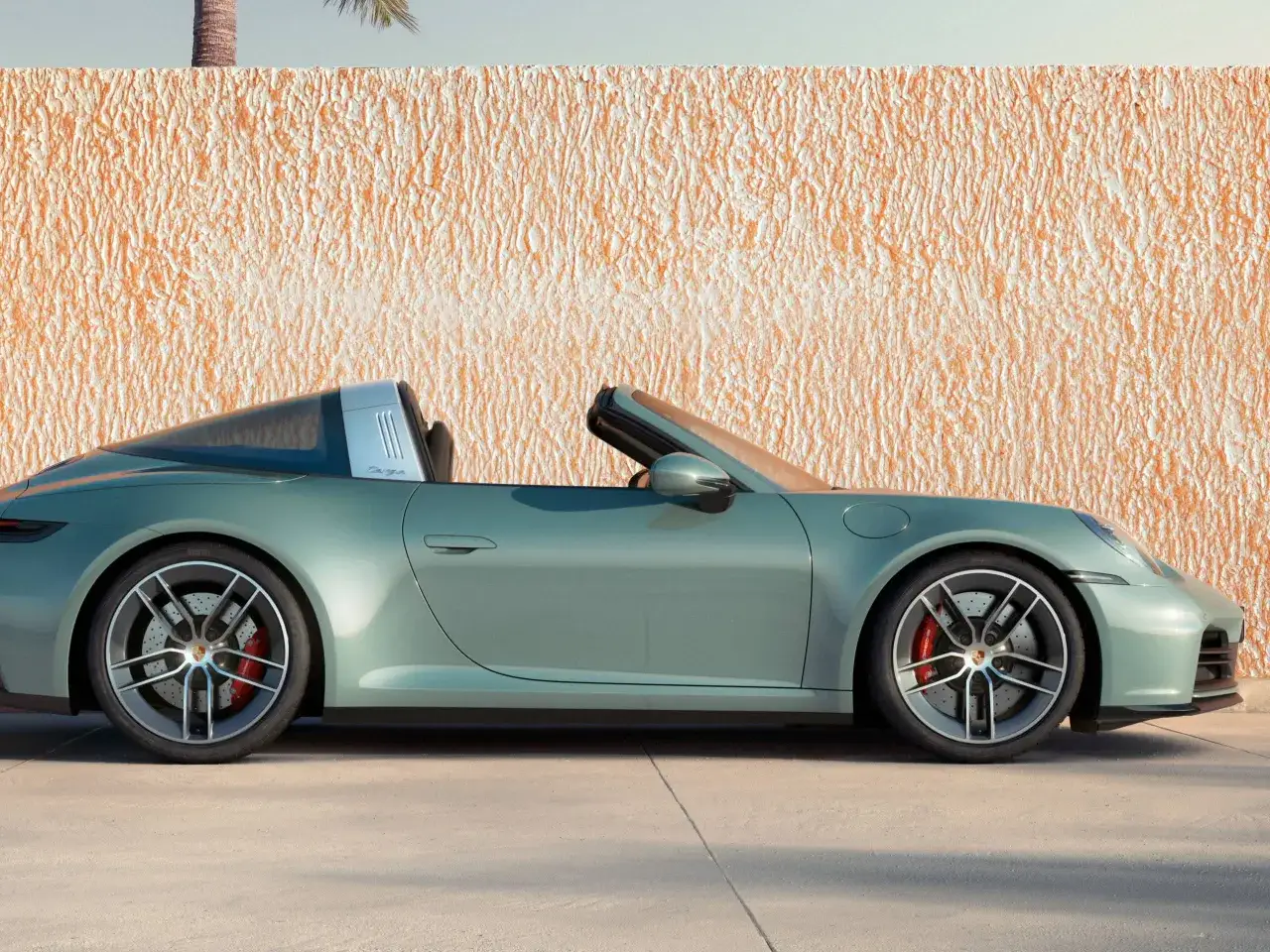 Zielony Porsche 911 Targa z otwartym dachem, zaparkowany przy pomarańczowej, chropowatej ścianie.