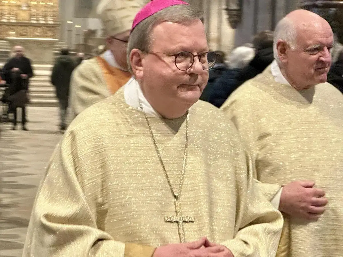 Bischof Bode tr&auml;gt eine goldene Messrobe und eine pinke Mitra. Er steht neben einem anderen Geistlichen in einer Kirche.