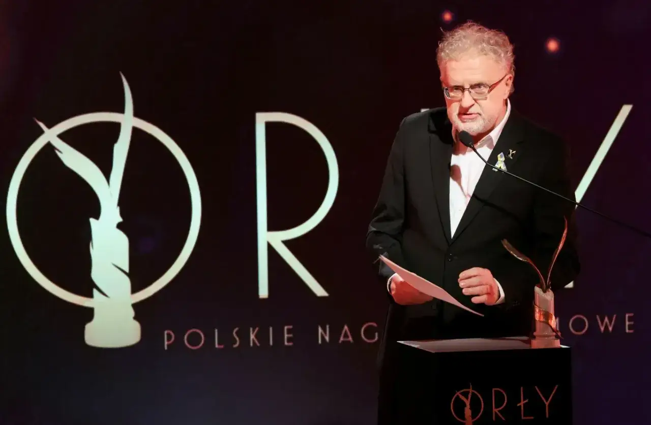 Mężczyzna w garniturze przemawia na scenie podczas gali Orłów, nagród Polskiego Instytutu Sztuki Filmowej.
