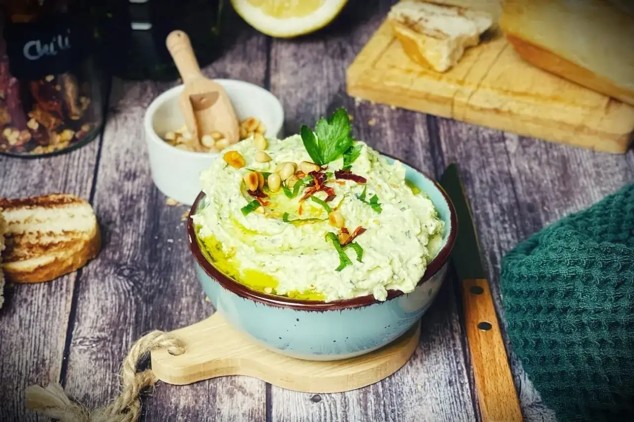 Cremiger Zucchini-Dip mit Pinienkernen und Kr&auml;utern, serviert mit ger&ouml;stetem Brot.