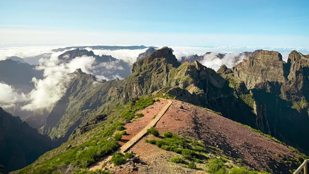 Atemberaubende Berglandschaft auf Madeira, mit Wolken, die sich durch zerklüftete Gipfel schlängeln. Ein Pfad führt über einen roten Hang, ein wahres Highlight von Madeira.