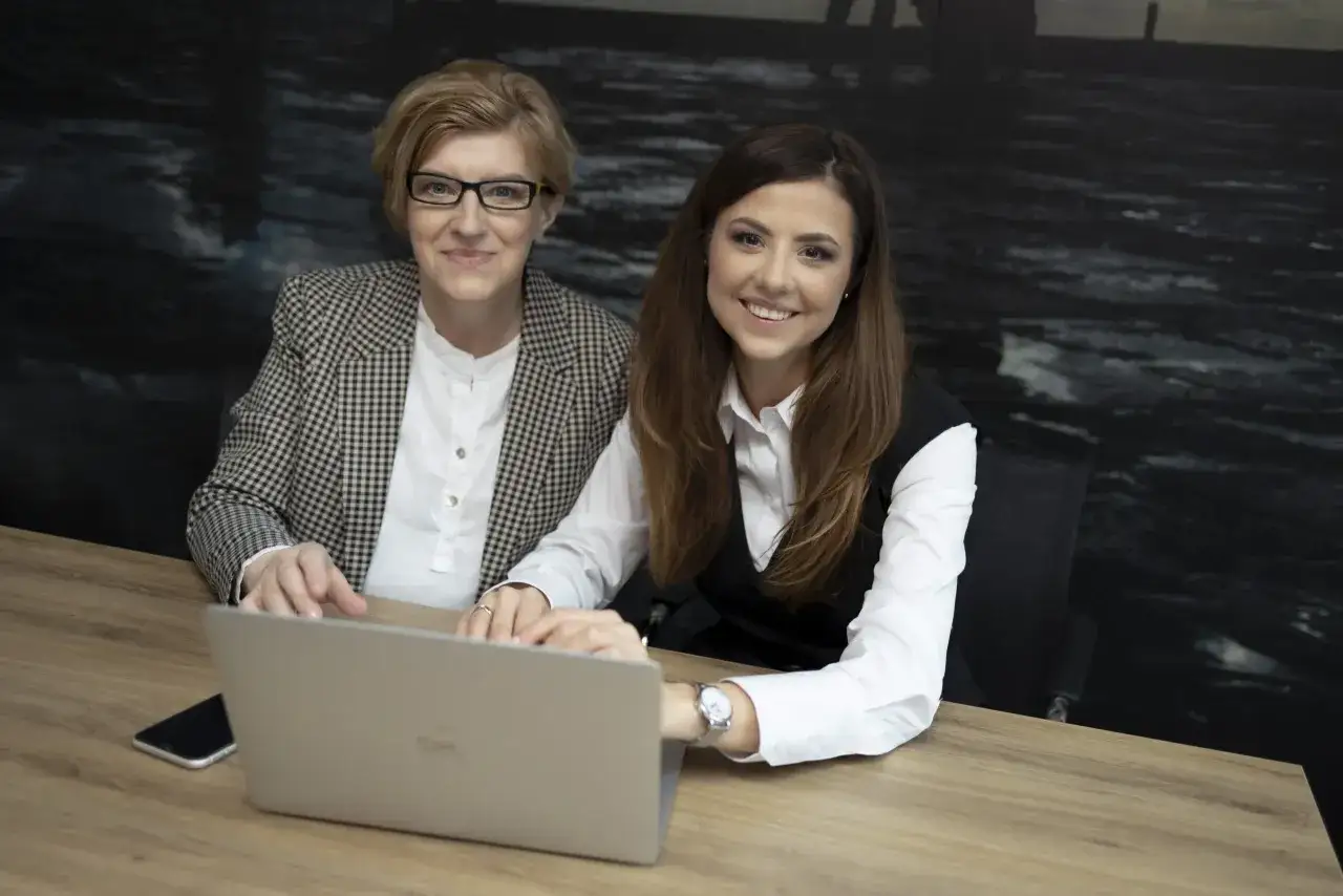Dwie kobiety w biurze przy biurku z laptopem i telefonem.