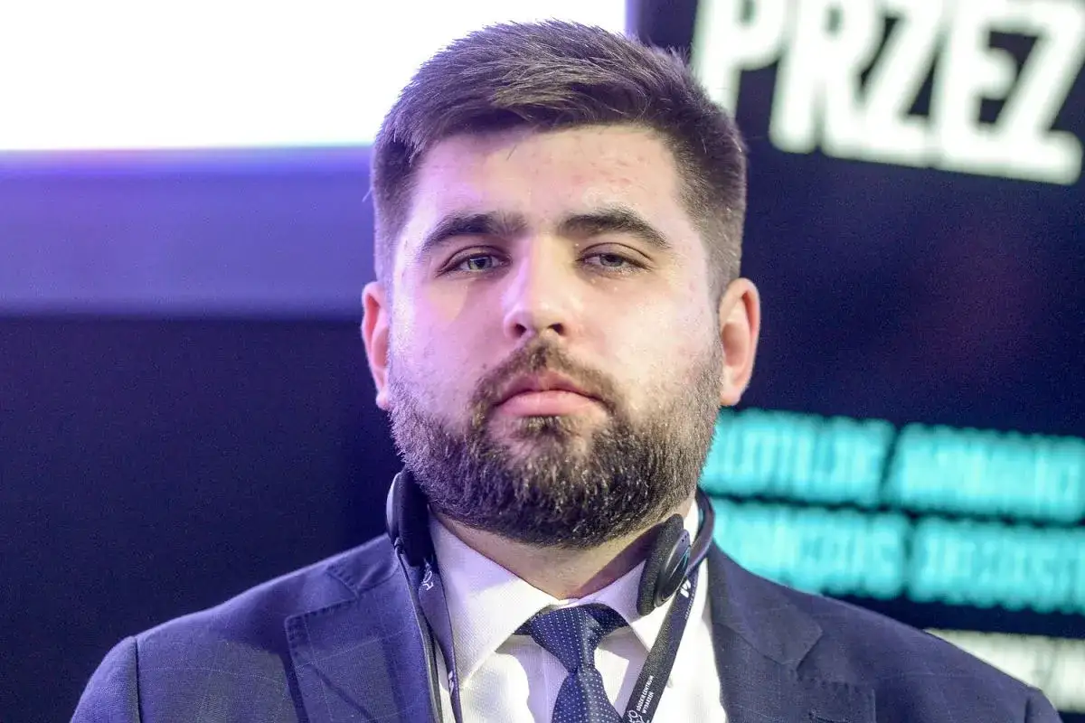Mężczyzna w garniturze z zarostem, słuchawkami na szyi. Działacze zaskoczeni, dlaczego kandydatura Jakuba Banaszka na premiera budzi emocje.