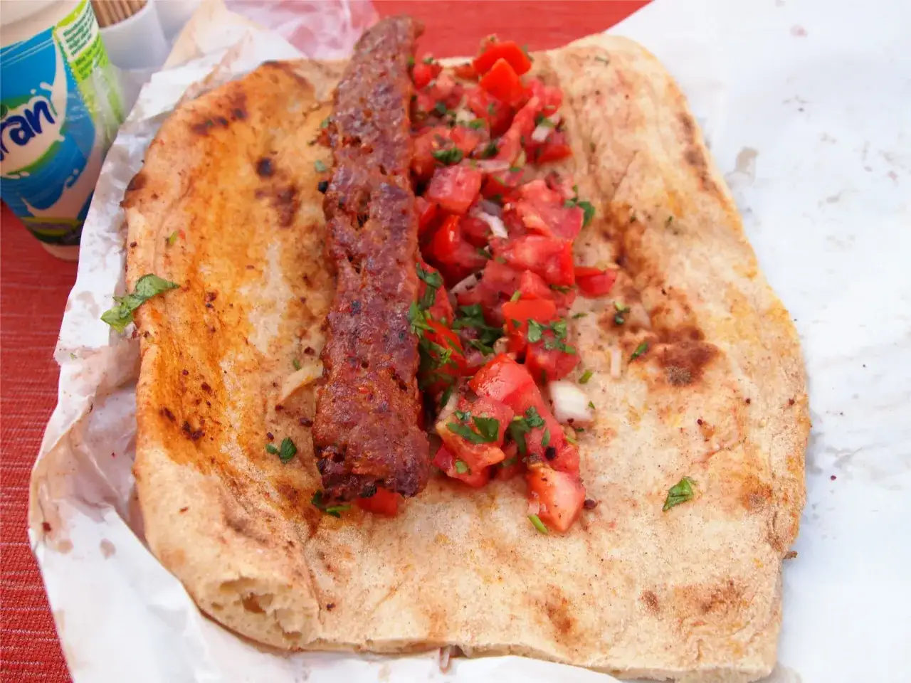 Prawdziwy kebab na chlebku z pomidorami i natką pietruszki. Obok kubek jogurtu.