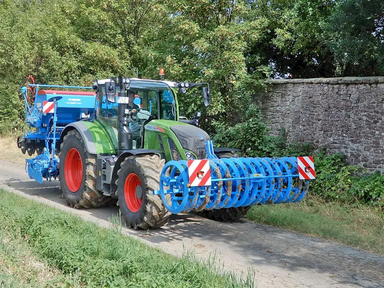 Gr&uuml;ner Traktor mit angeh&auml;ngter S&auml;maschine und Bodenwalze. Die Bodenwalze hat eine Warnafel halterung mit rot-wei&szlig;en Warnstreifen.