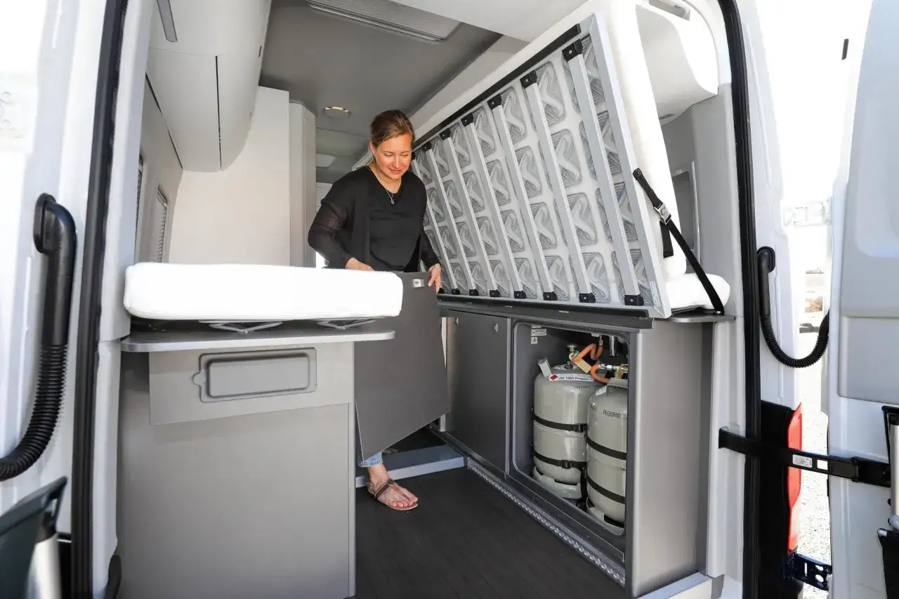 Interior de una Volkswagen California con baño, mostrando la cama desplegada y los tanques de propano.