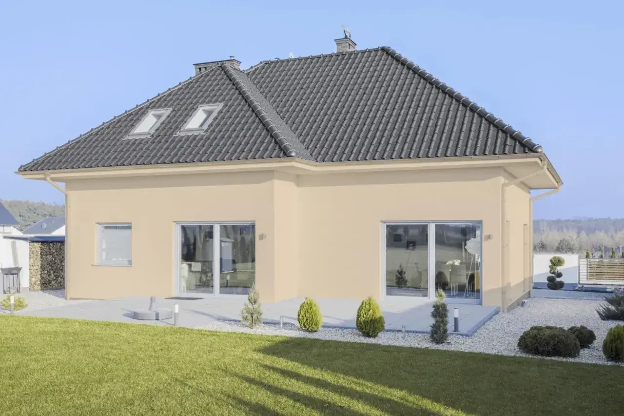 Maison moderne avec une **couleur de fa&ccedil;ade maison tendance** beige clair, toit sombre, grandes fen&ecirc;tres et jardin verdoyant.