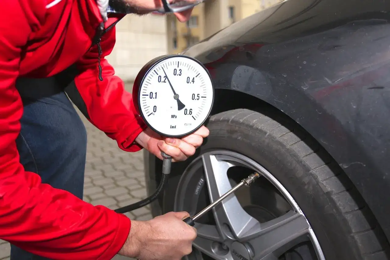 Sprawdzanie ciśnienia w oponach Renault Laguna 3. Mężczyzna w czerwonej kurtce używa manometru do pomiaru ciśnienia w kole.