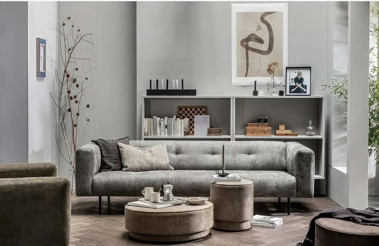 En stilren soffgrupp med en grå soffa, två fåtöljer och en rund sittpall. En mysig inredning med böcker, konst och växter.