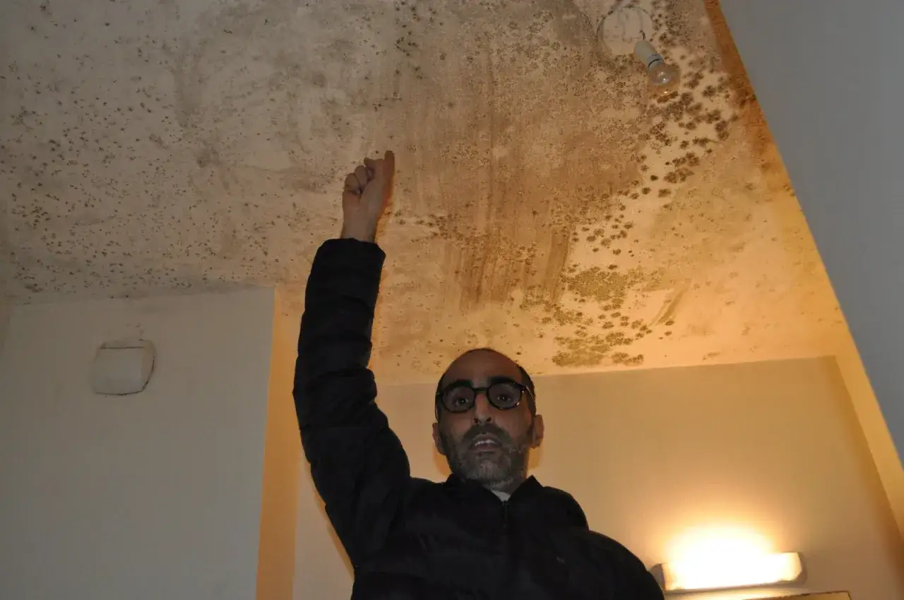 Un homme pointe du doigt le plafond moisi, t&eacute;moignant d'un logement insalubre.