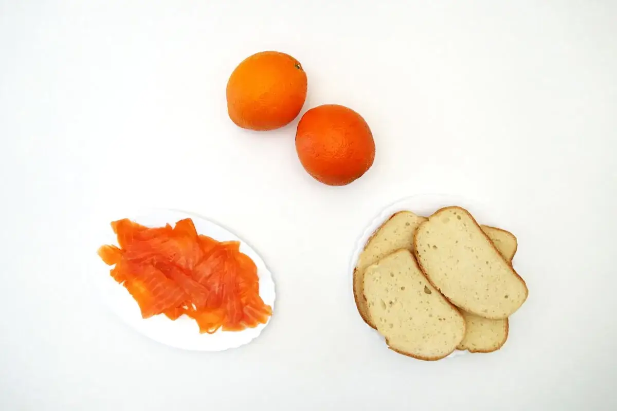 Dos naranjas, rebanadas de pan y un plato con salm&oacute;n ahumado, listos para un delicioso aperitivo.