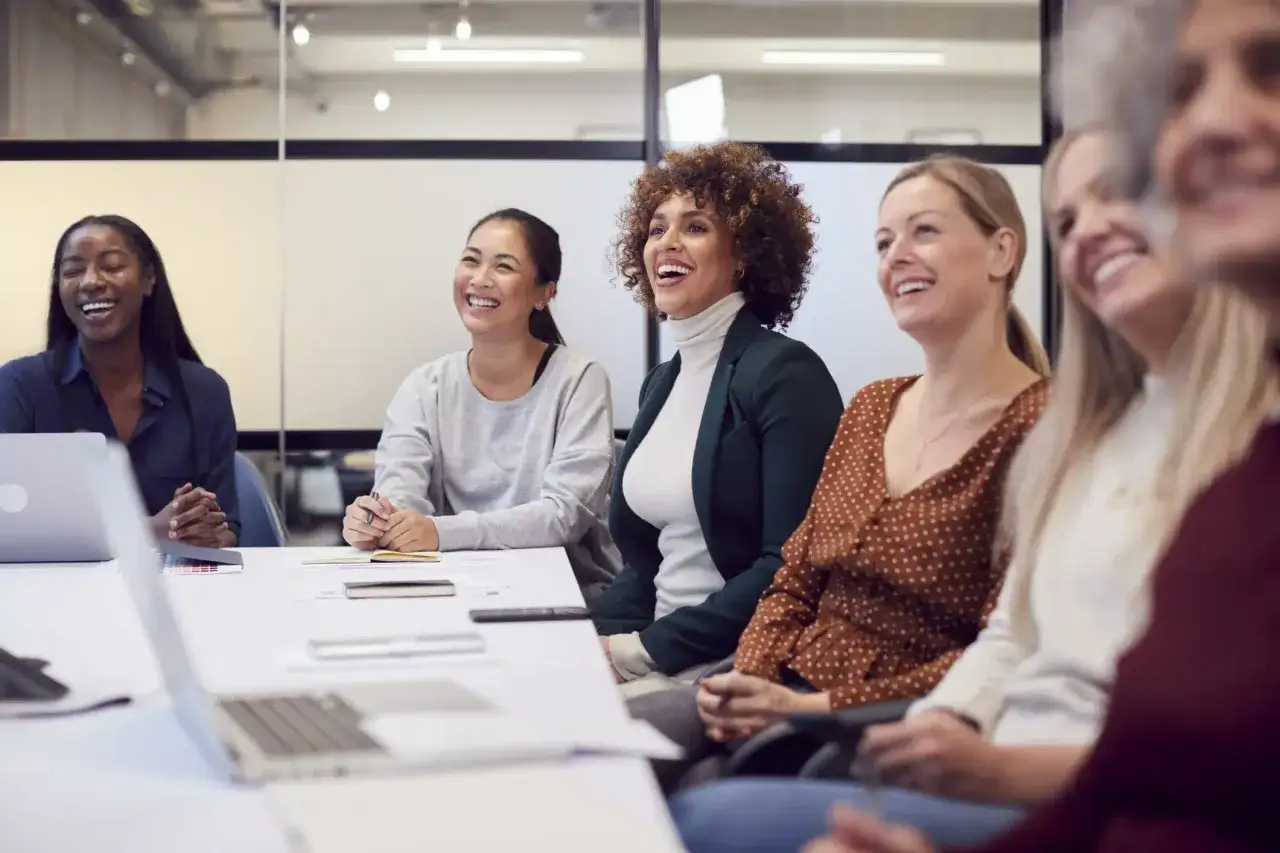 Diverse group of women laughing during emotional intelligence training for managers.