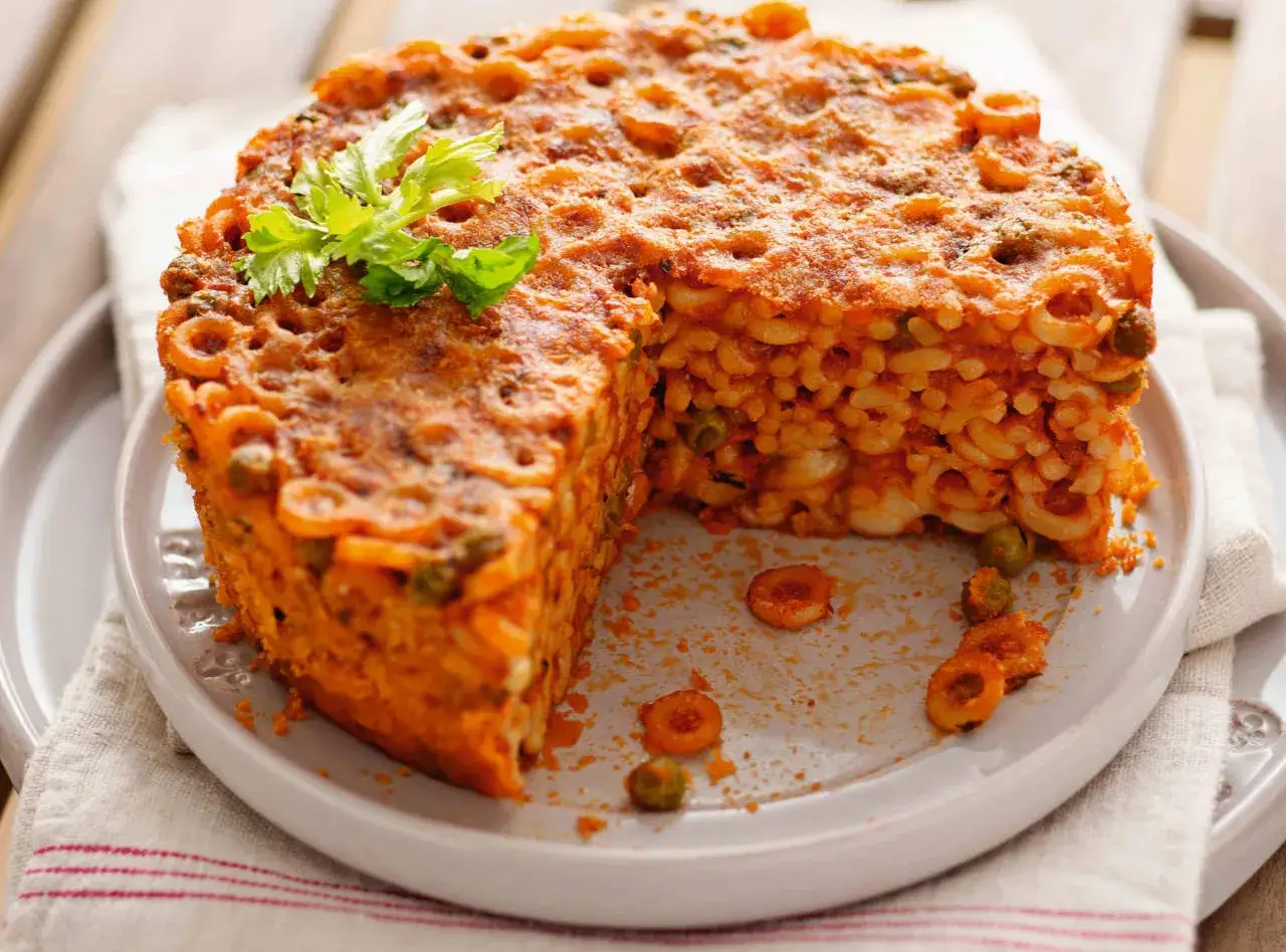 Un tortino di anelletti al forno, dorato e invitante, con piselli e un rametto di prezzemolo.