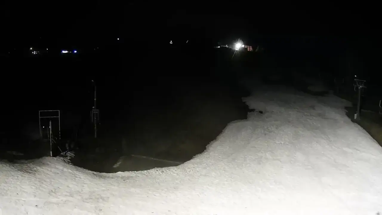 Nocne widoki z kamer na Olczańskim Wierchu. Ośnieżony stok i wyciąg narciarski w ciemnościach.