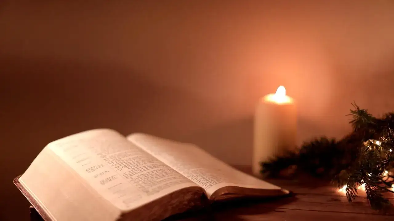 Otwarta Biblia, płonąca świeca i gałązka choinki tworzą nastrój do szukania pocieszających cytatów z Biblii.
