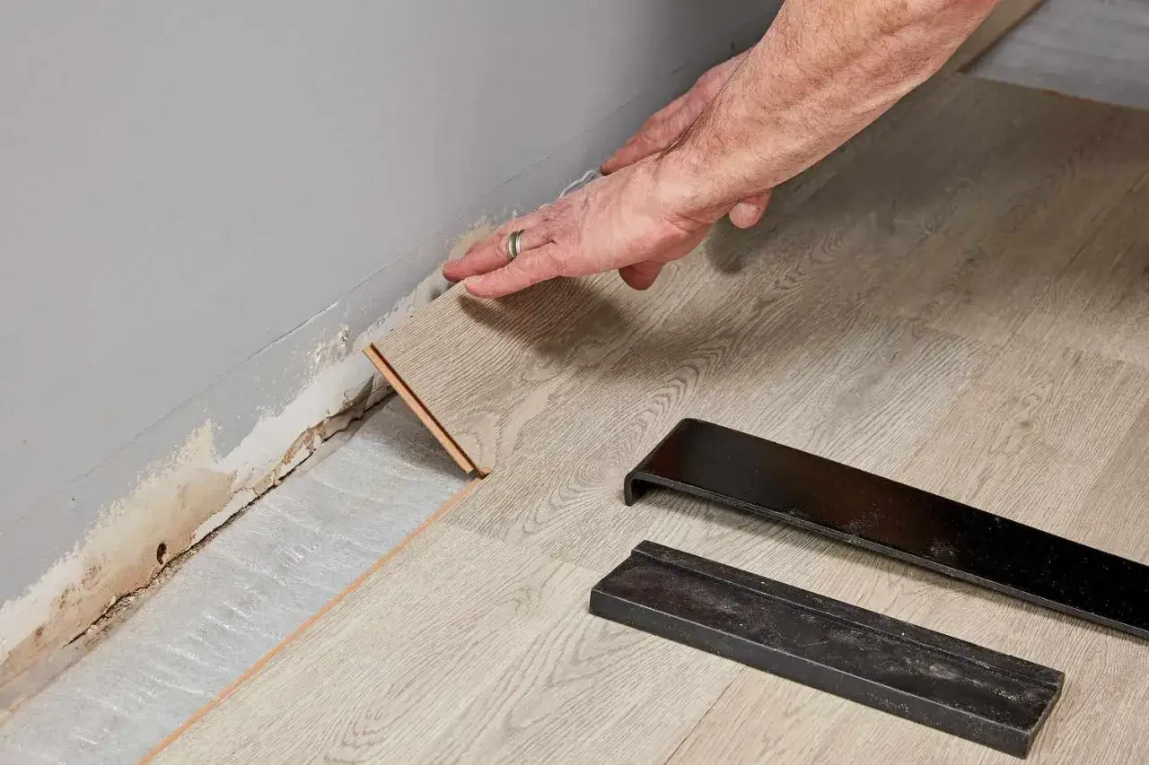 Pose d'une lame de parquet flottant contre le mur, avec des outils pour aider à comment couper du parquet flottant.