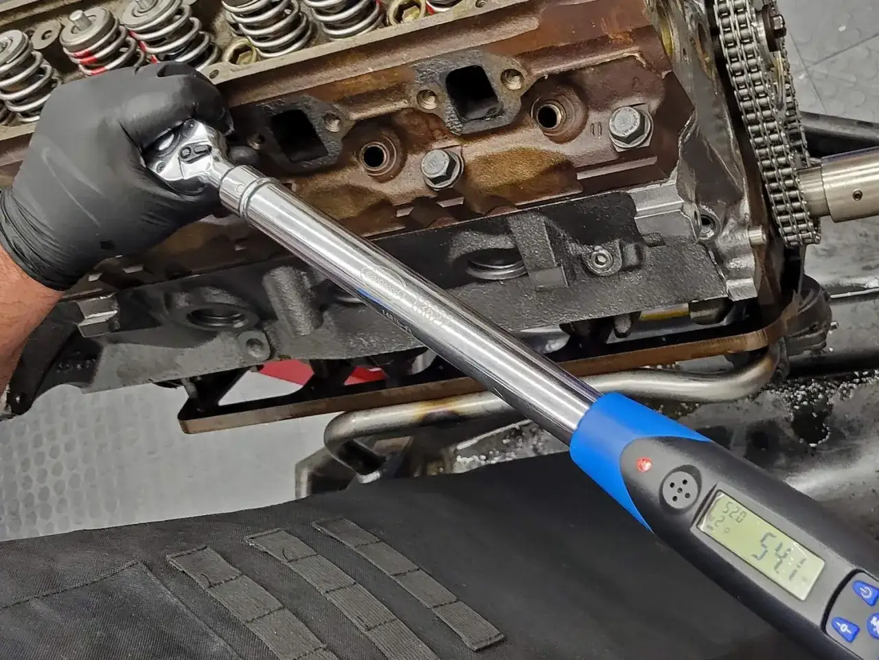 Mano con guante negro usa llave dinamométrica para ajustar tornillos de motor. Aprende como saber el par de apriete de un tornillo.