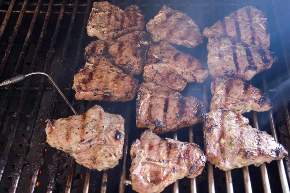 Saftige Lammkoteletts brutzeln auf dem Grill. Ein Thermometer steckt in einem Stück, um den perfekten Gargrad zu prüfen. Das Lamm grillen ist eine Kunst!