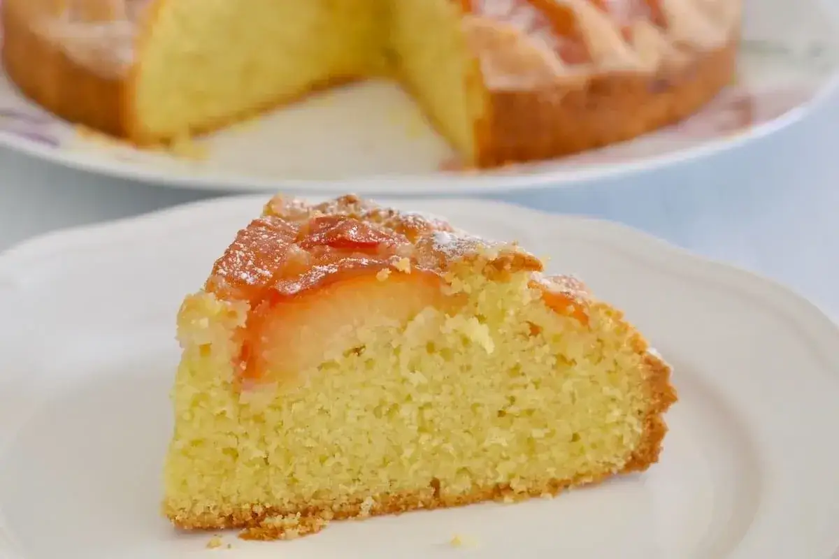 Una fetta di torta soffice con prugne fresche, cosparsa di zucchero a velo.