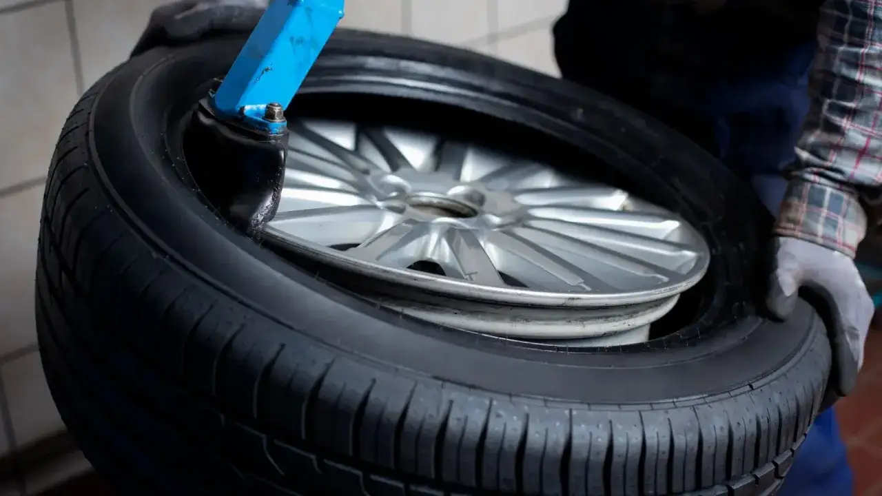 Mechanik w rękawiczkach trzyma oponę z felgą, przygotowując się do wymiany. Zastanawiasz się, ile kosztuje wymiana opon?