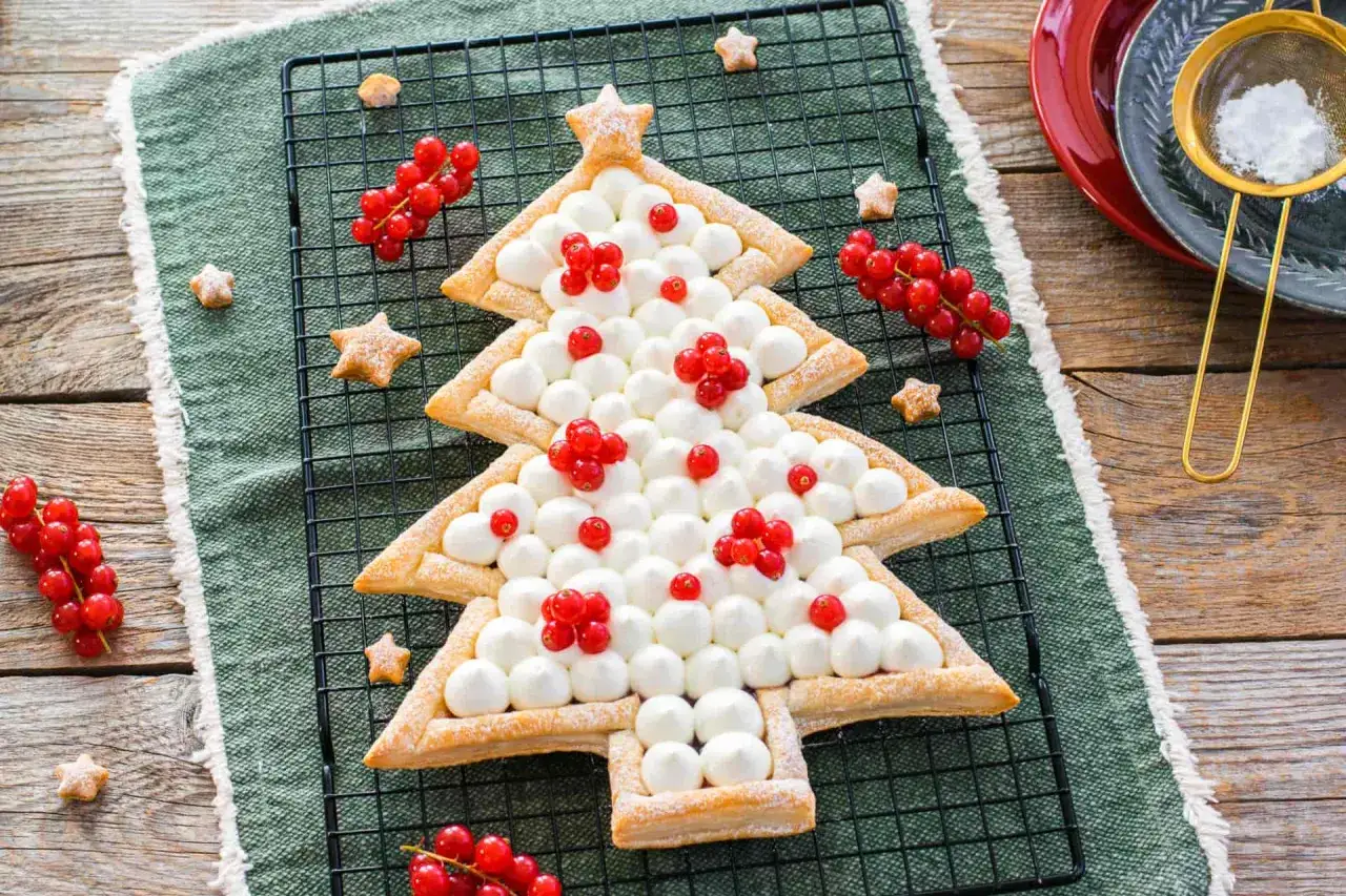Un delizioso dolce a forma di albero di Natale, decorato con panna montata e ribes rossi, pronto per le feste.