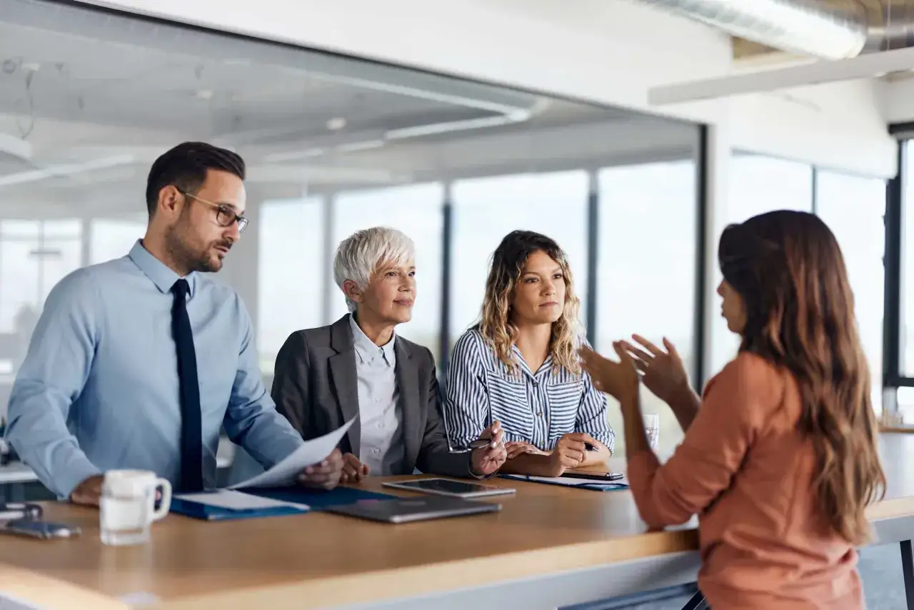 Colloquio di lavoro: tre persone sedute a un tavolo, una candidata parla mentre due selezionatori ascoltano attentamente. Un passo importante per cambiare lavoro.