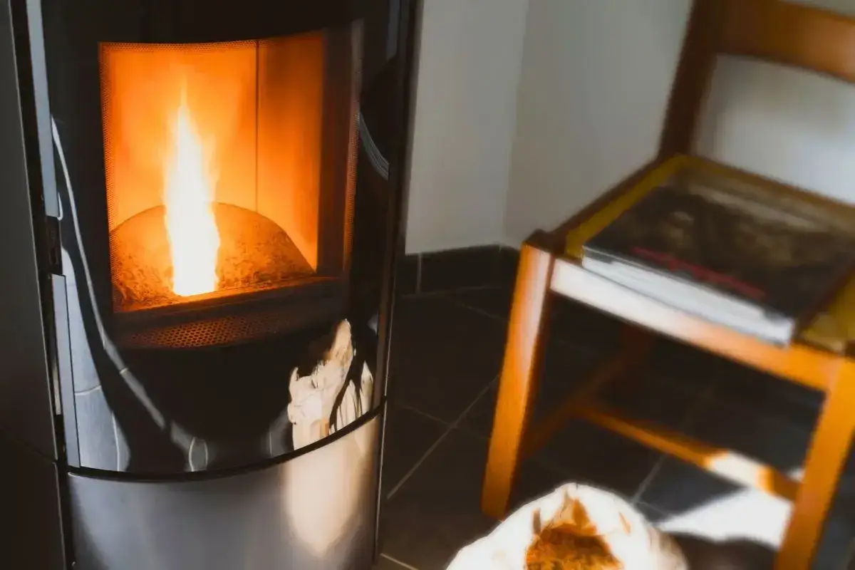 Poêle à granulés Superior en marche, flamme vive. Une chaise en bois avec un livre à côté.
