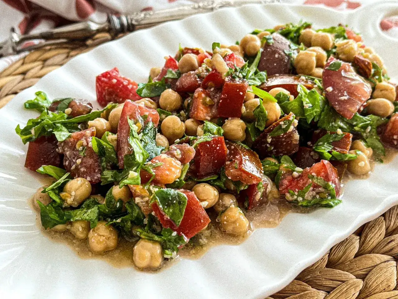 Mediterraner Salat mit Kichererbsen, Tomaten, Rucola und getrockneten Tomaten, appetitlich auf einem wei&szlig;en Teller angerichtet.