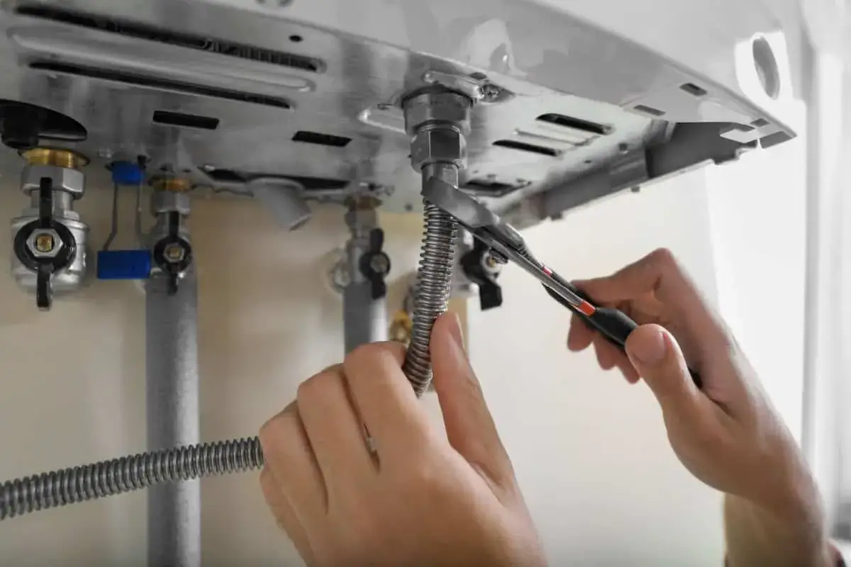 Mani che stringono un tubo flessibile con una pinza, forse per risolvere il problema dello scaldabagno a batteria non si accende.