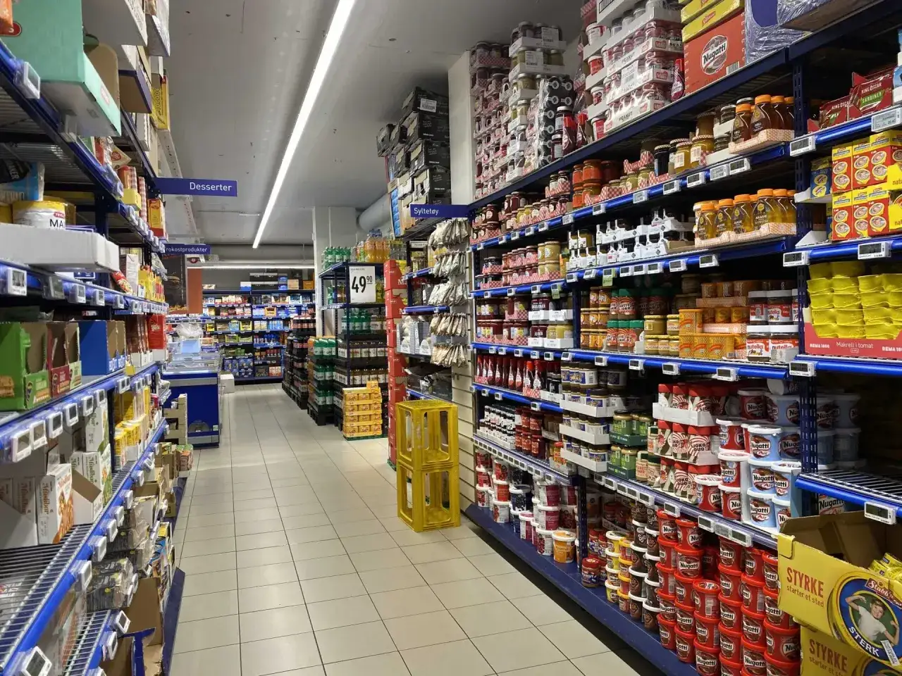 Słoiki z dżemami i pastami na półkach sklepowych, pokazujące ceny jedzenia w Norwegii.