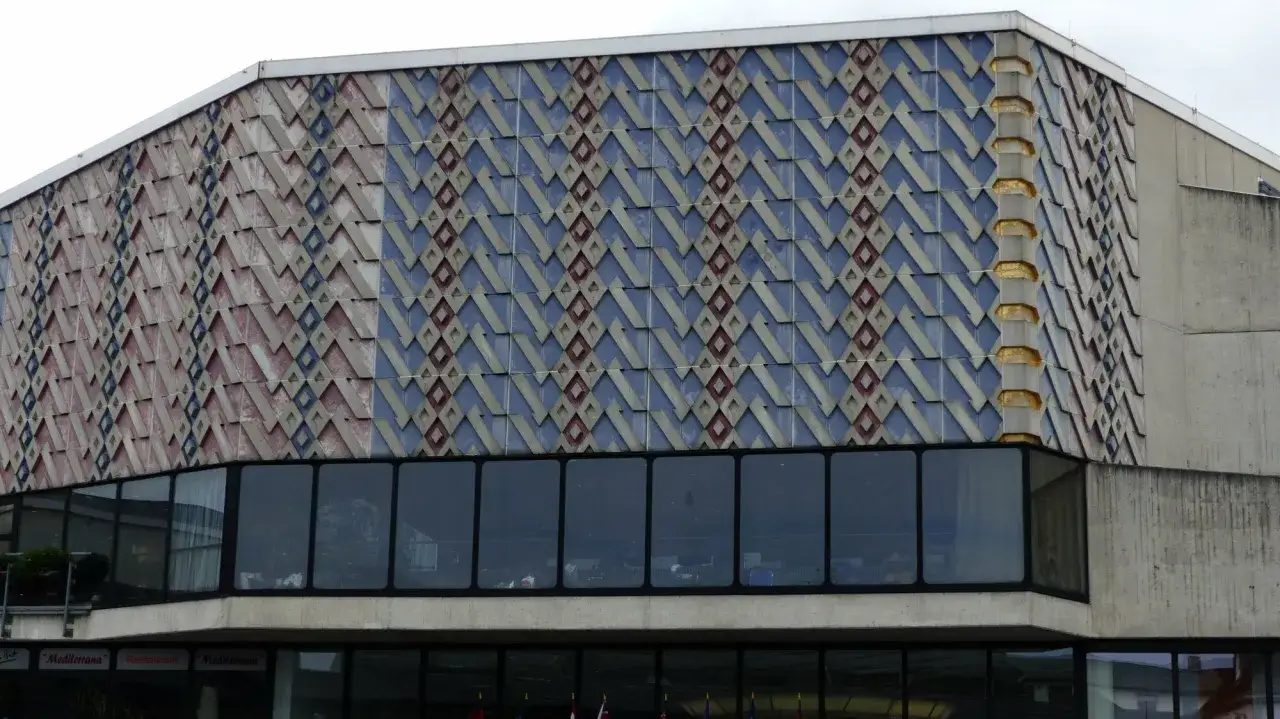 Fassade der Stadthalle Hilpoltstein mit geometrischem Muster in Blau, Rot und Grau. Gro&szlig;e Fensterfront im unteren Bereich.