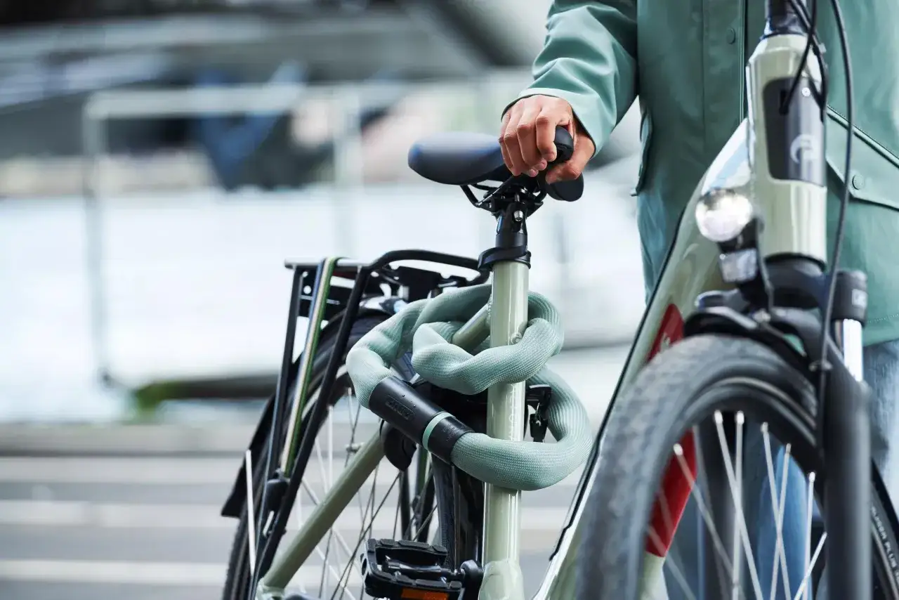 Een persoon met een groen jack zet een fiets op slot met een stevig slot, om fietsen diefstal te voorkomen.