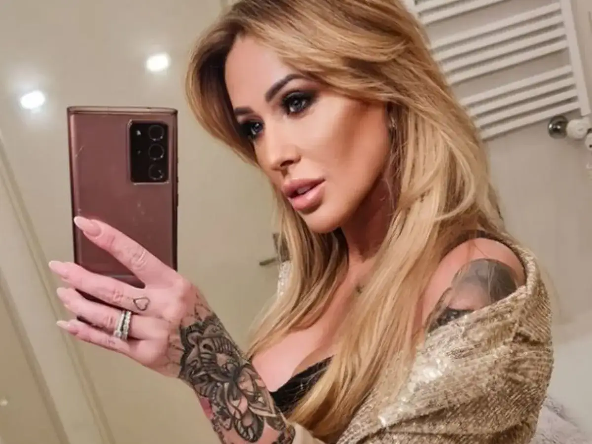Sylwia Peretti robi selfie, prezentując tatuaże na ręce i ramię, złoty żakiet i makijaż.