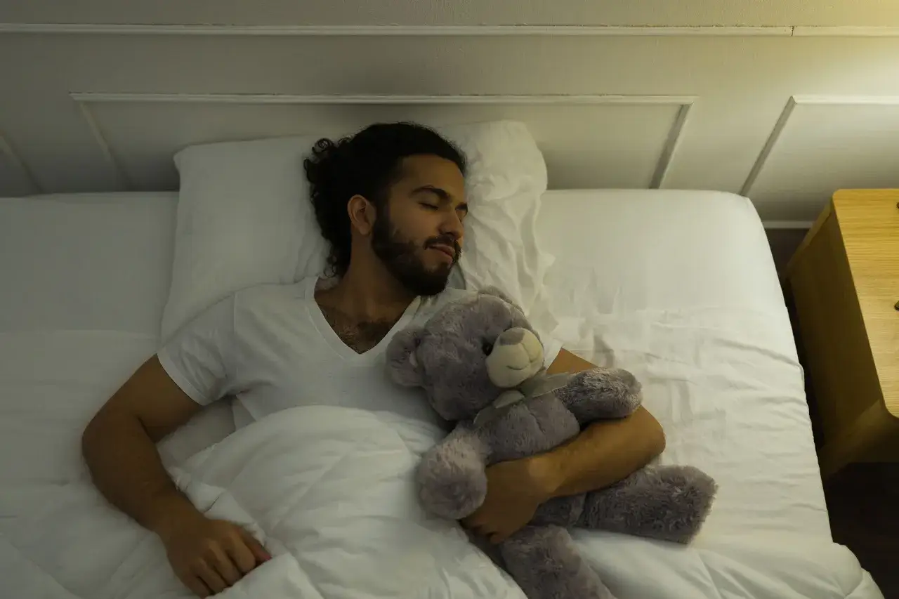 Ein Mann schläft friedlich mit einem Teddybär. Kuscheltiere können auch für Erwachsene psychologische Unterstützung bieten.