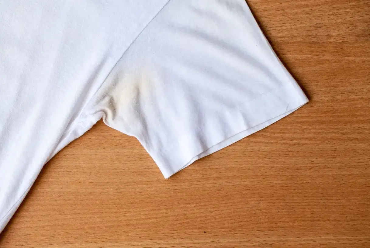 T-shirt blanc avec une tache jaune sous le bras, un signe de transpiration tenace.