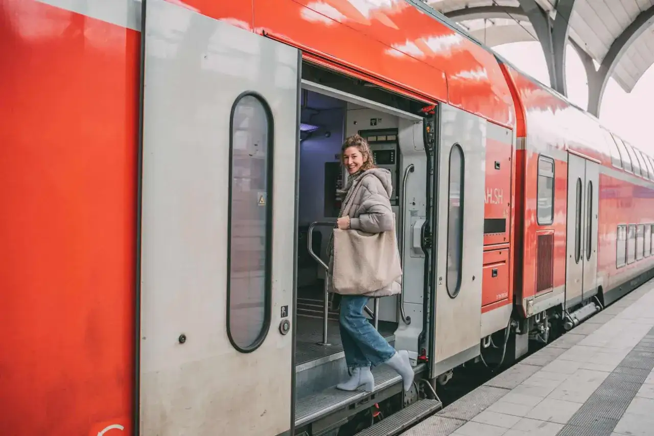 Frau steigt in roten Zug ein, bereit für die Reise mit dem Zug ans Meer.