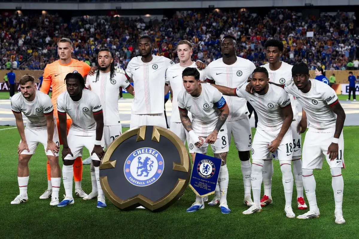 Drużyna piłkarzy Chelsea w białych strojach pozuje do zdjęcia z herbem klubu.