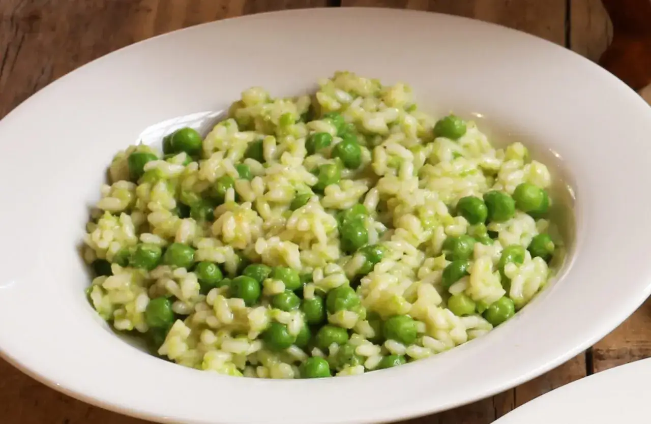 Un cremoso piatto di risi e bisi, con piselli freschi e riso carnaroli, servito in una ciotola bianca.