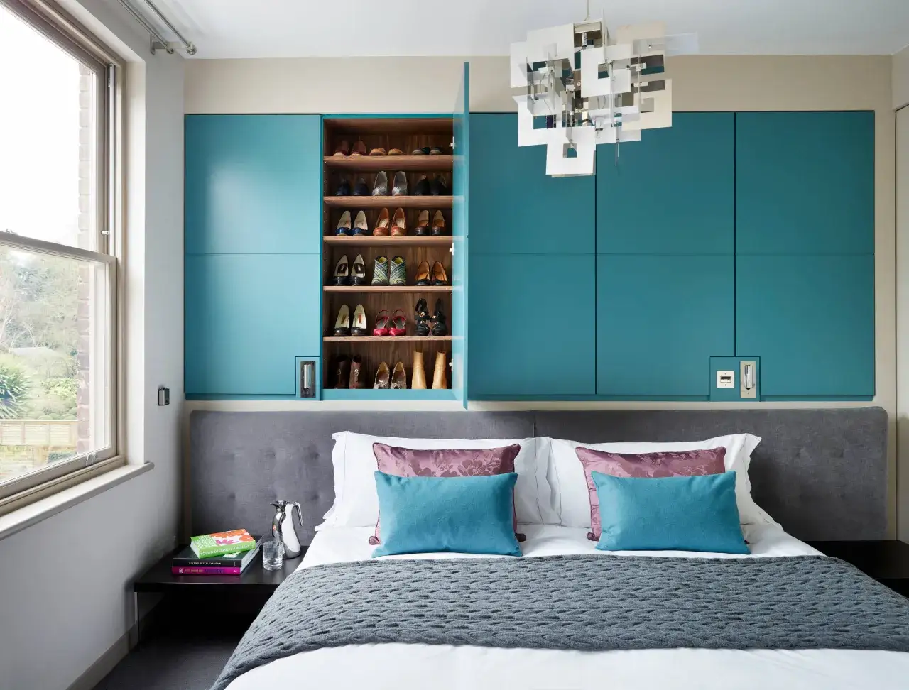 Ein Schlafzimmer mit einem Bett, das mit Kissen und einer Decke dekoriert ist. Ein offener Schrank zeigt ordentlich aufbewahrte Schuhe.