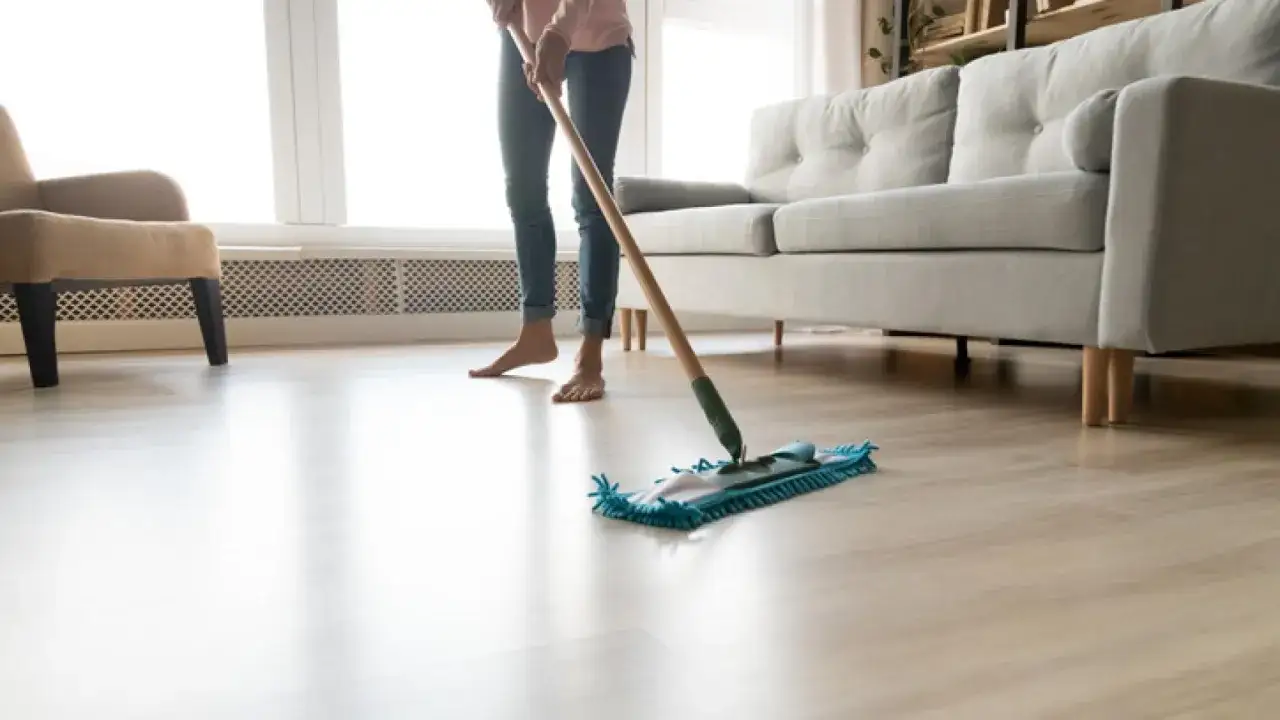 Persona limpiando el suelo de madera con una mopa, dejando un brillo impecable en el sal&oacute;n.
