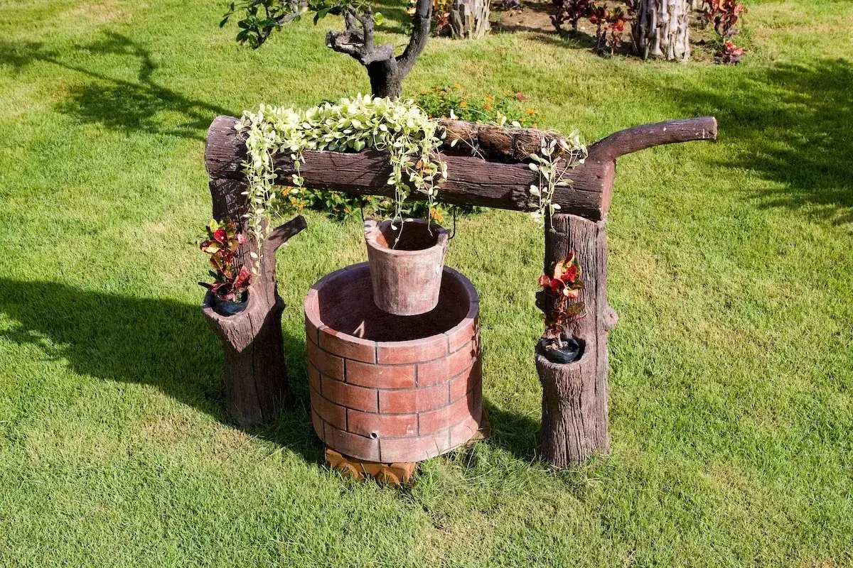Pozzo decorativo in mattoni con secchio appeso, circondato da erba verde. Chissà quanto costa fare un pozzo così!