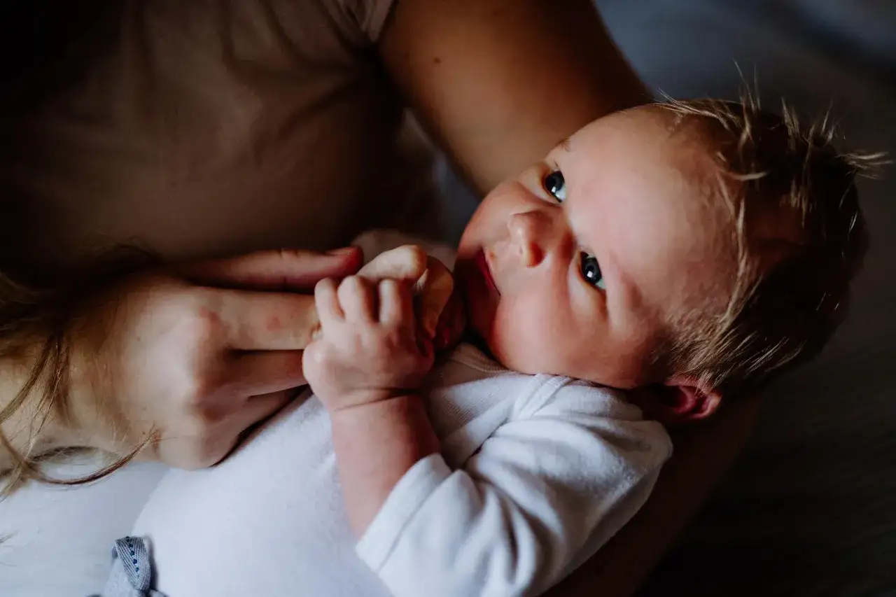 Dziecko w ramionach mamy, jego mała rączka ściska palec. Wczesne wykrycie chorób metabolicznych, jak fenyloketonuria, daje szansę na zdrowe życie.