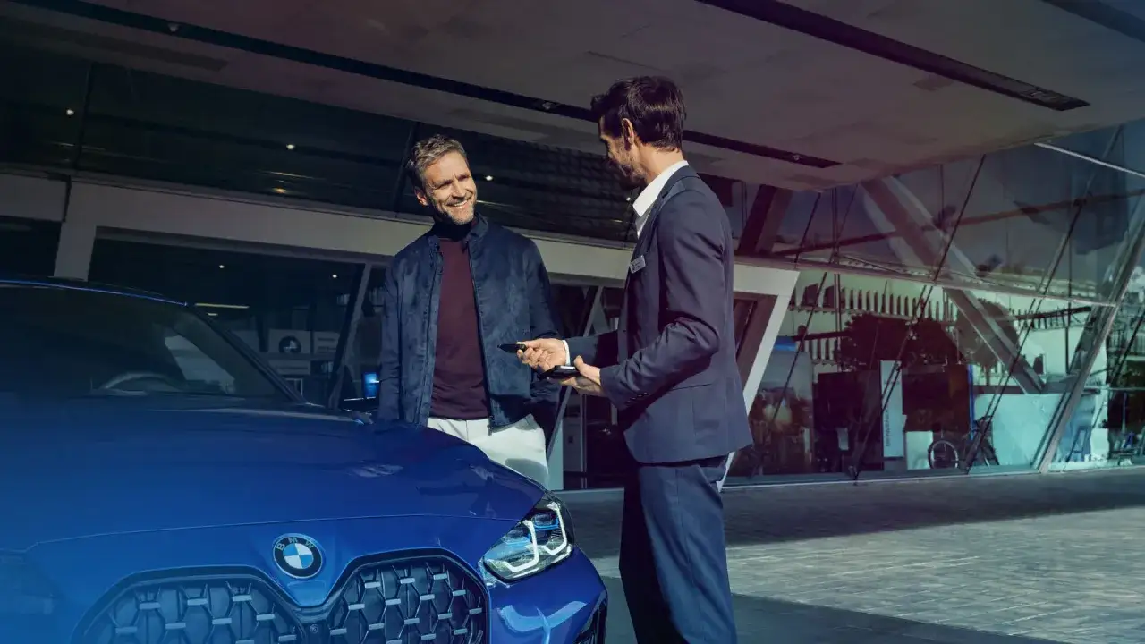 Sprzedawca w salonie samochodowym przekazuje kluczyki do nowego BMW. Ciekawe, ile zarabia sprzedawca w salonie samochodowym za takie transakcje.