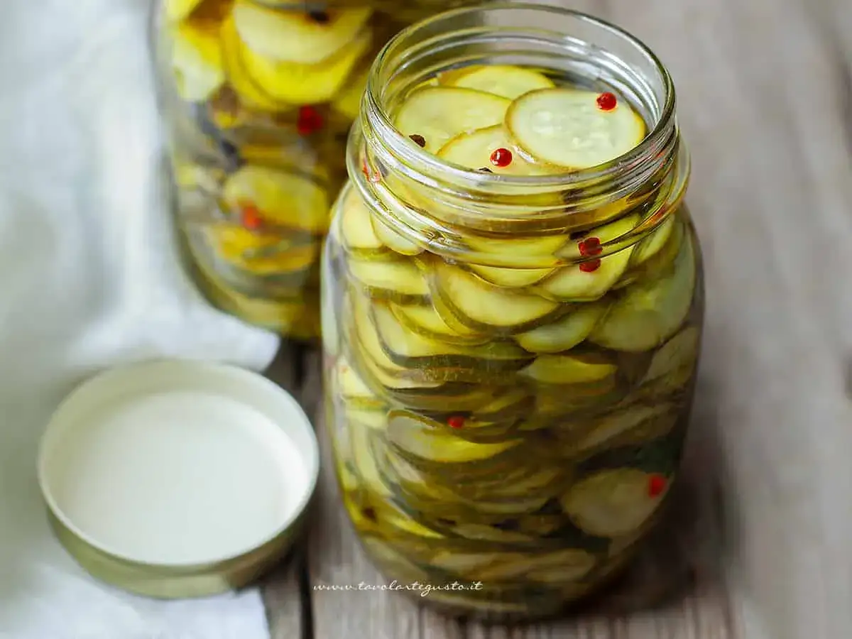 Barattoli pieni di zucchine sott'olio, affettate finemente e conservate in olio, con qualche grano di pepe rosa.
