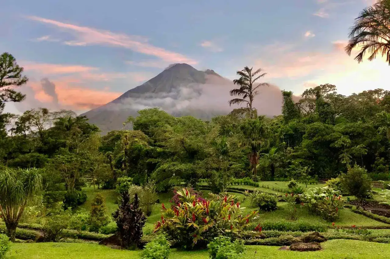 En frodig tr&auml;dg&aring;rd med f&auml;rgglada blommor och en molnt&auml;ckt vulkan i bakgrunden, en vy fr&aring;n Costa Rica.