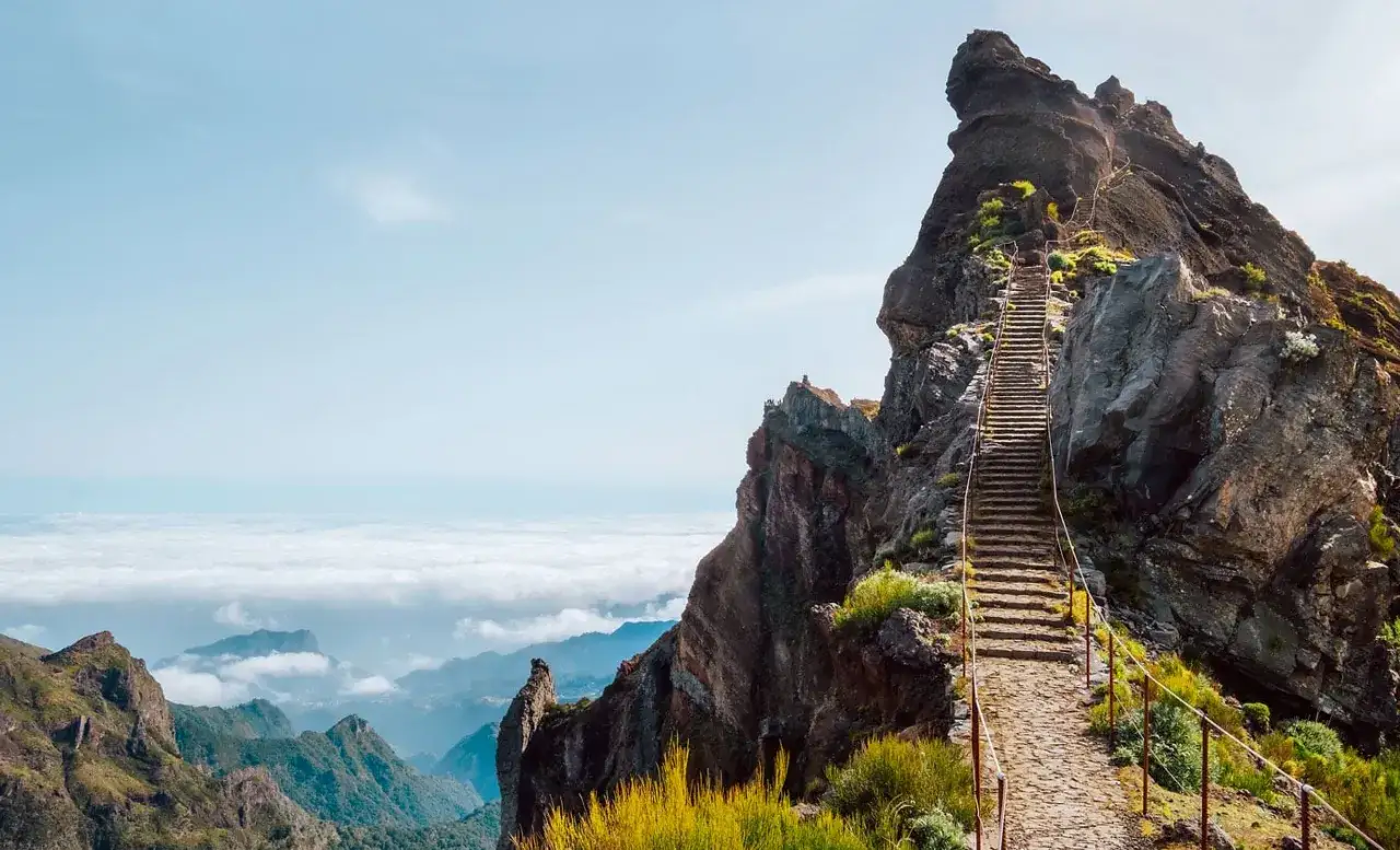 Steile Steintreppe führt auf einen Felsen, ein Muss auf Madeira. Wolkenmeer unter blauem Himmel.
