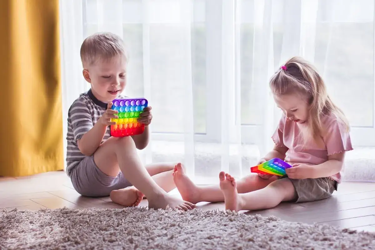 Chłopiec i dziewczynka bawią się tęczowymi zabawkami sensorycznymi. Uważne obserwowanie ich zachowań może pomóc w rozpoznaniu objawów autyzmu u 3 latka.