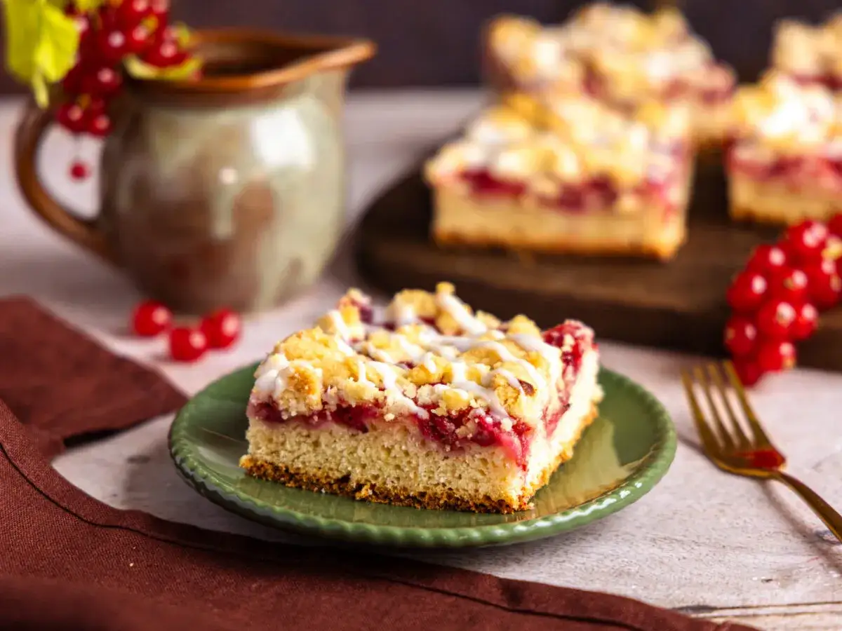 Saftiger Johannisbeerkuchen mit Streuseln, wie ihn Landfrauen backen. Ein St&uuml;ck auf gr&uuml;nem Teller, daneben rote Johannisbeeren.