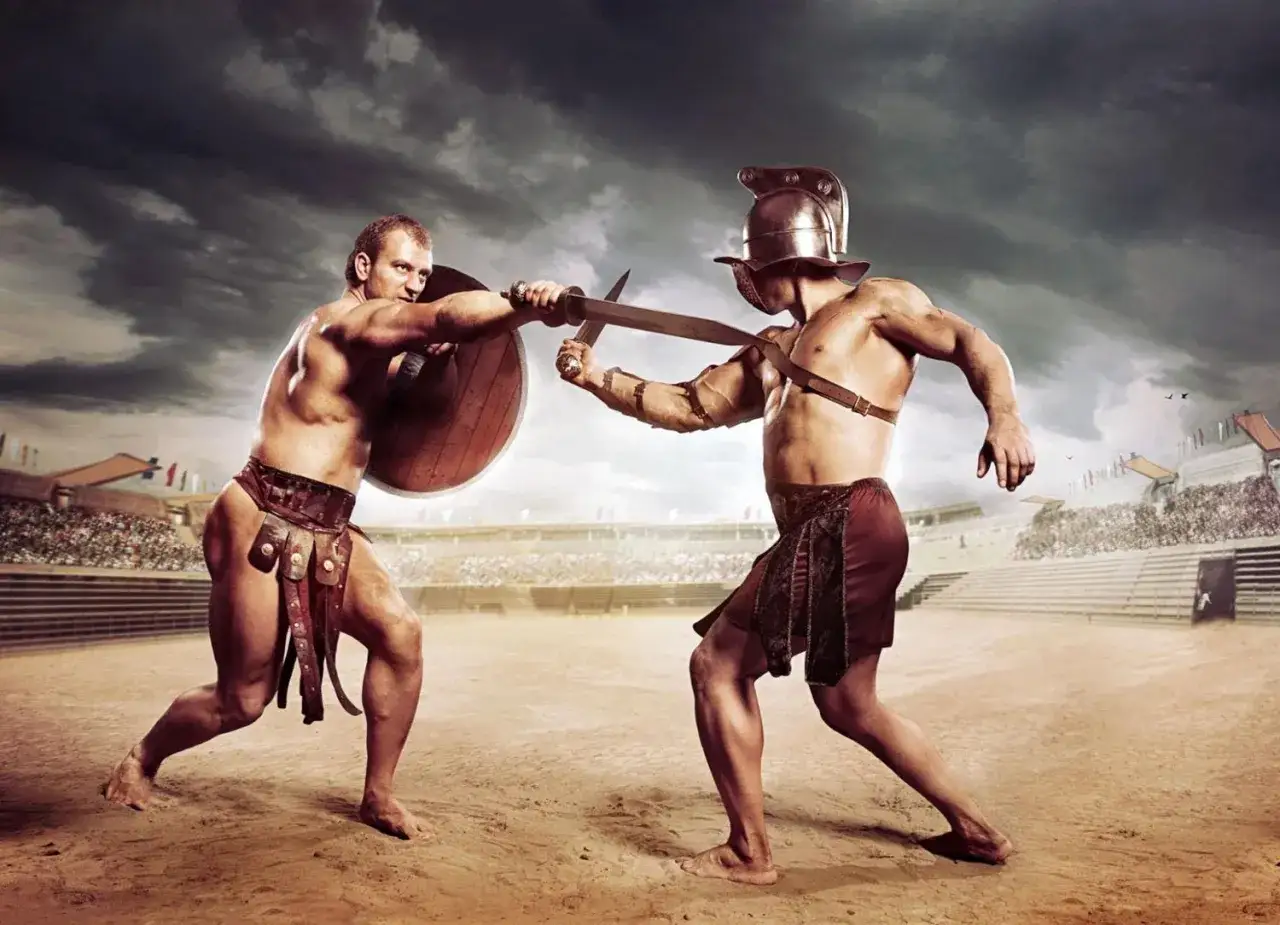 Zwei Gladiatoren k&auml;mpfen in einer Arena. Sie tragen R&uuml;stungen und Waffen. Das zeigt, was ein Gladiator war: ein K&auml;mpfer im antiken Rom.